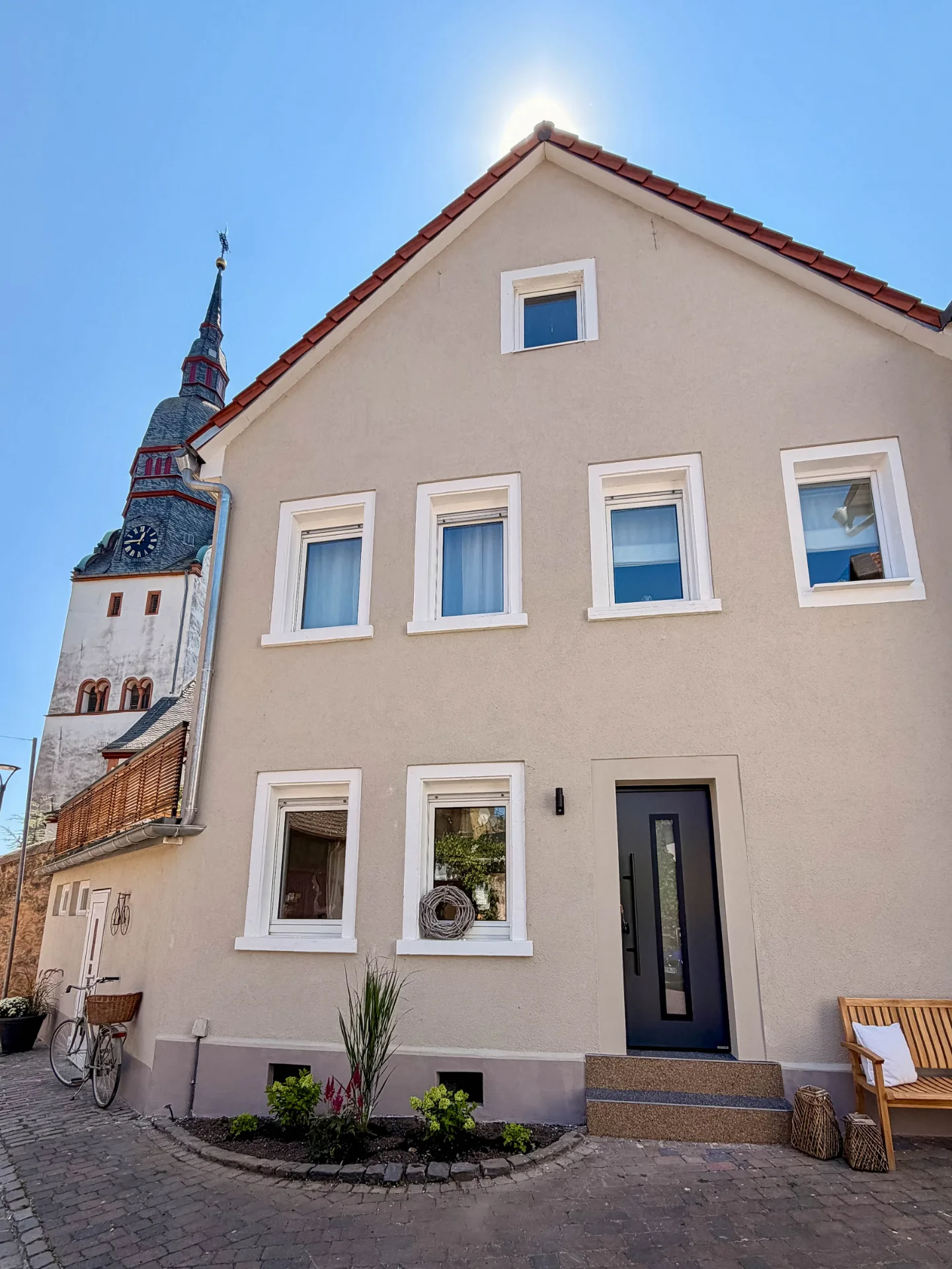Außenansicht des Markt Quartiers in Nierstein mit Eingangsbereich, Sitzbank und Kirchturm direkt neben dem Haus.
