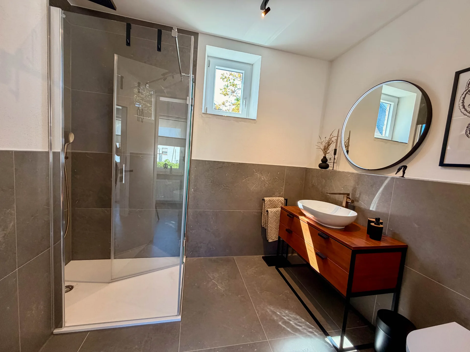 Modernes Badezimmer des Markt Quartiers in Nierstein mit Dusche, Fenster, Aufsatzwaschbecken und rundem Spiegel.