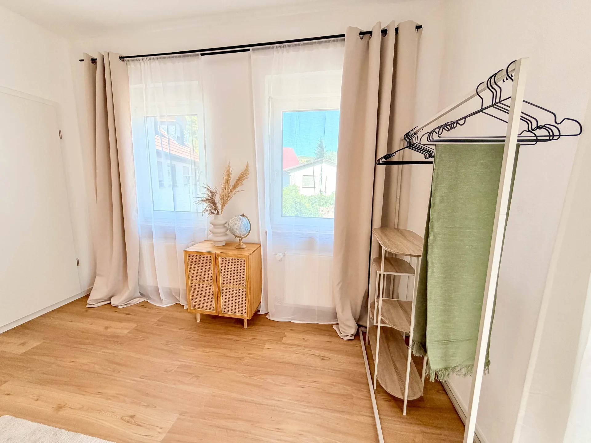 Fensterbereich des Schlafzimmers im Markt Quartier mit Kleiderstange, Ablage, Kommode und Holzboden.
