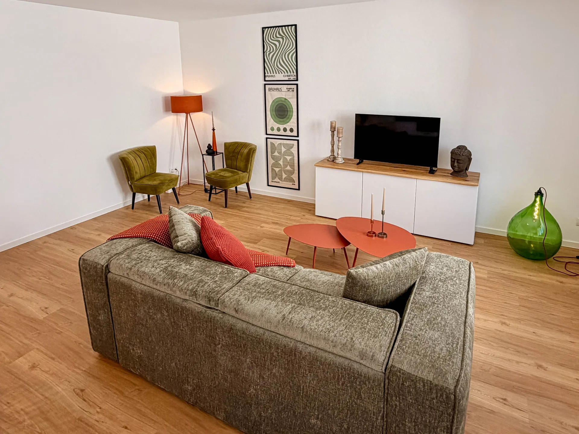 Wohnzimmer des Markt Quartiers in Nierstein mit großem Sofa, Fernseher, roten Couchtischen und grüner Glasleuchte.